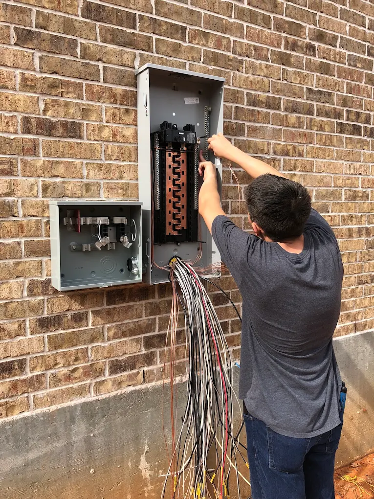 Lowe Home Electric electrician wiring a new residential breaker panel on a brick home in Montgomery, TX